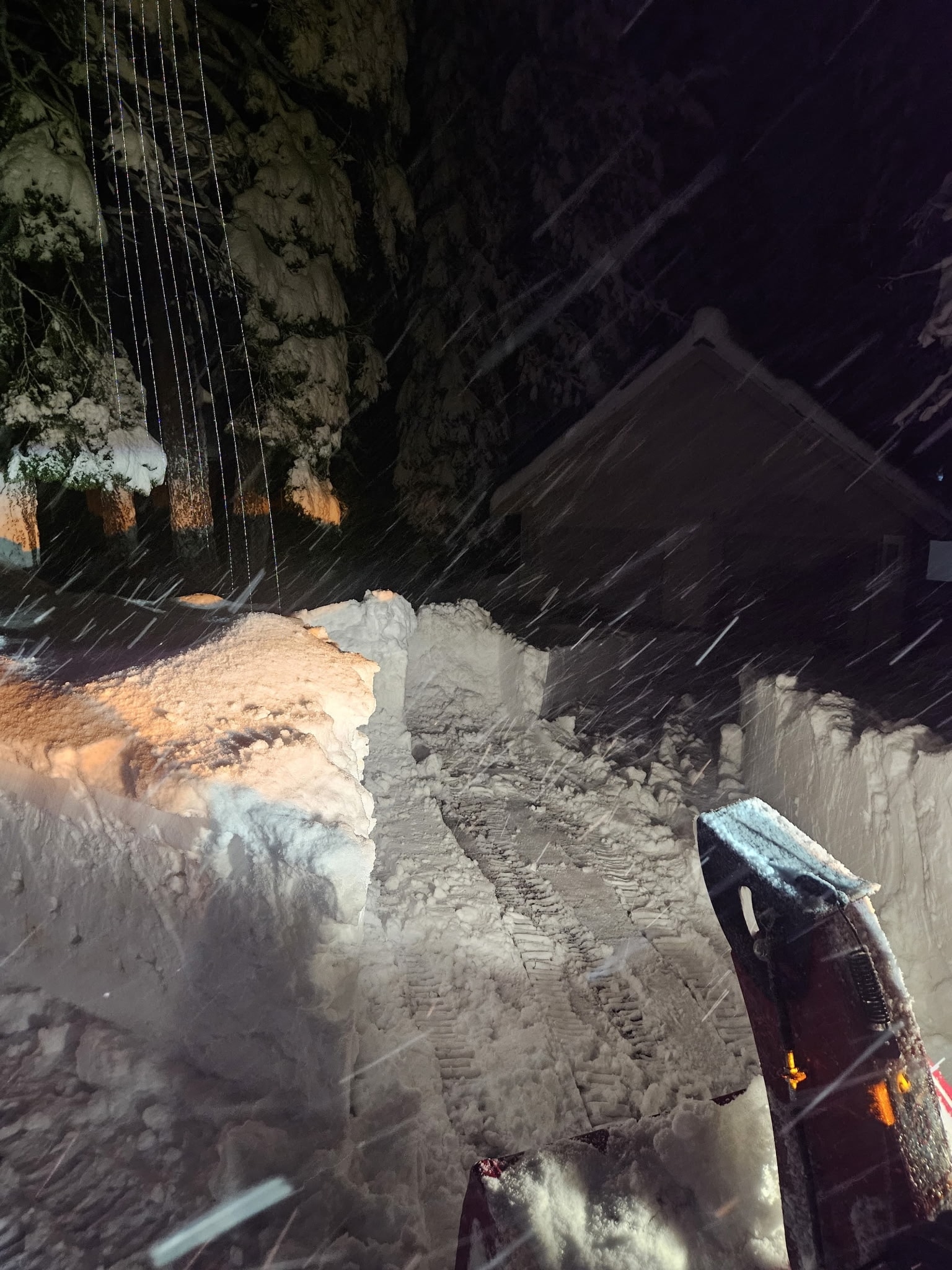 Plow blade clearing a snow-packed driveway at night during a storm